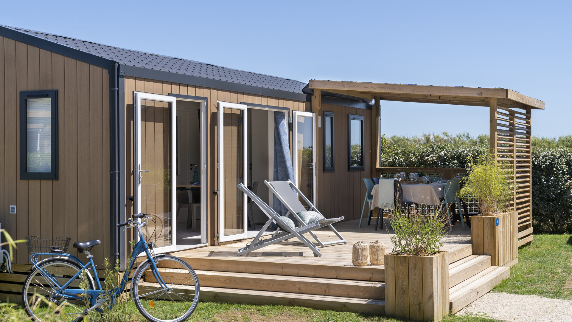 Maison mobile avec terrasse en bois et vélo bleu.